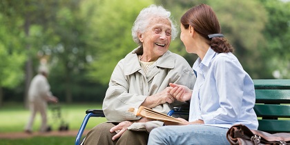 Senior lady and a carer sitting together on a park bench.