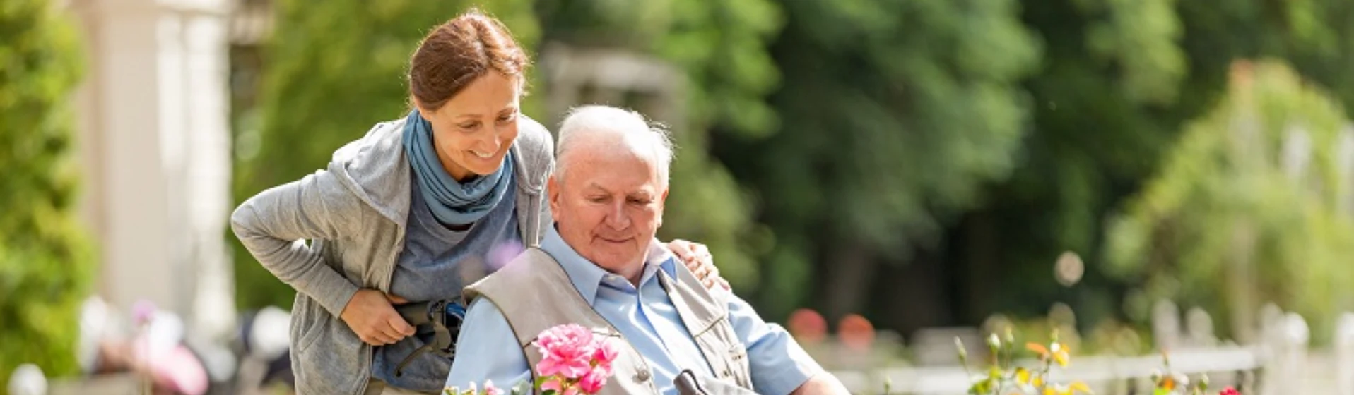 A senior resident enjoying the garden while siting in a wheelchair and being pushed by his relative