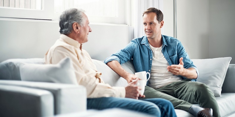 Shot of a young man and his elderly father having a chat over coffee on the sofa at home